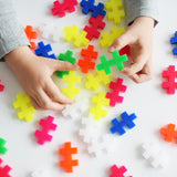 Child's hands piecing together colorful Plus-Plus BIG neon interlocking blocks on a white surface.