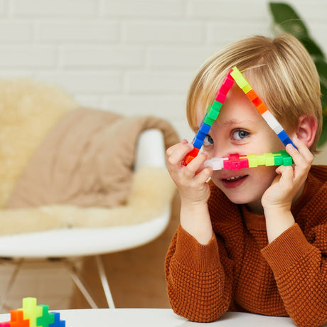 Child peeking through a triangle made of colorful Plus-Plus BIG building blocks.
