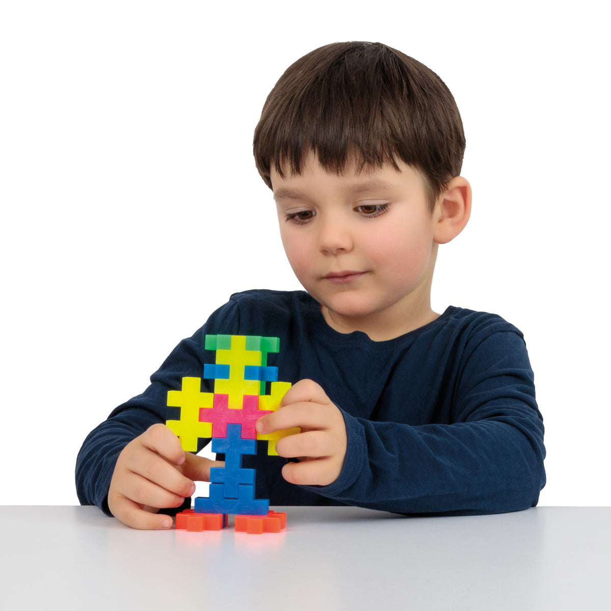 Young boy building a figure with colorful Plus-Plus BIG blocks on a white table.