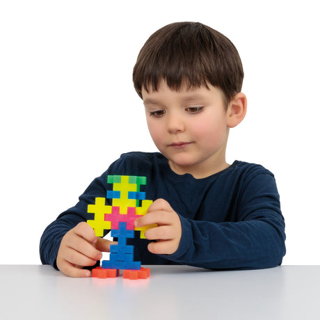 Young boy building a figure with colorful Plus-Plus BIG blocks on a white table.