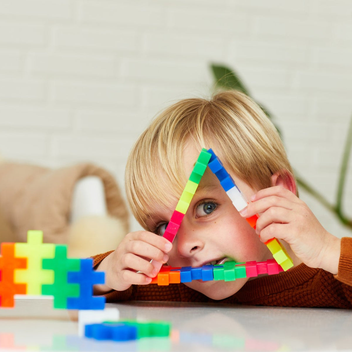 Young boy looking through a triangle shape made of colorful Plus-Plus BIG building blocks.