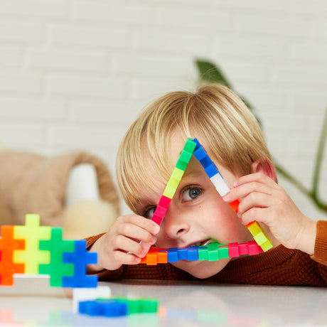 Young boy looking through a triangle shape made of colorful Plus-Plus BIG building blocks.