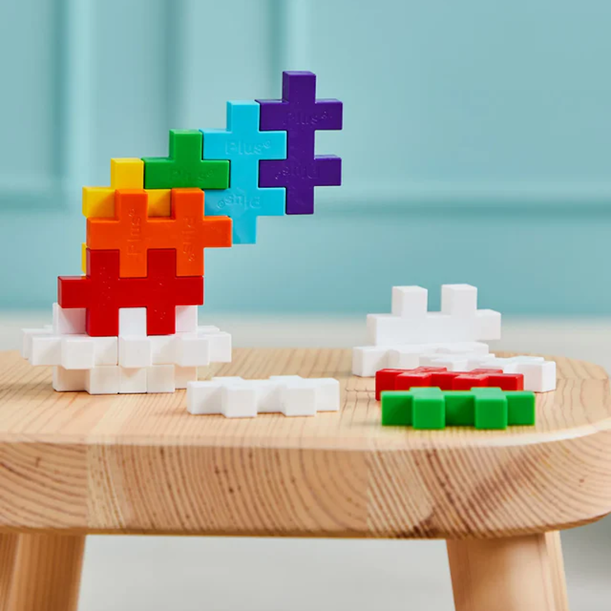Colorful interlocking puzzle pieces stacked on a wooden table against a light blue wall. Brightly colored blocks create a playful, creative scene.