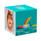 A colorful packaging box against a white background features a smiling child wearing multicolored puzzle pieces on their head. The box shows a rainbow with clouds and scattered puzzle blocks on a teal backdrop, suggesting fun and creativity.
