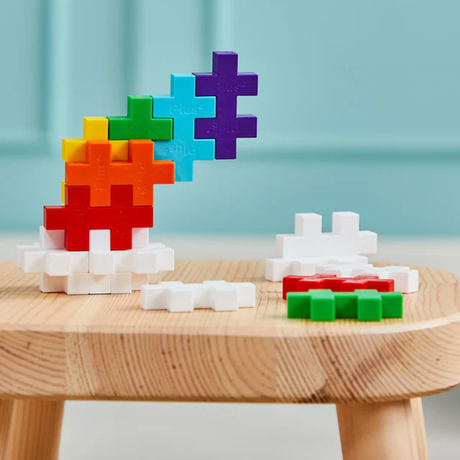 Colorful interlocking plus-shaped building blocks are stacked in a balanced arc on a wooden table, creating a playful and creative scene.