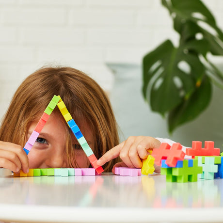 Child peering through a triangle made of colorful Plus-Plus BIG tropical blocks.