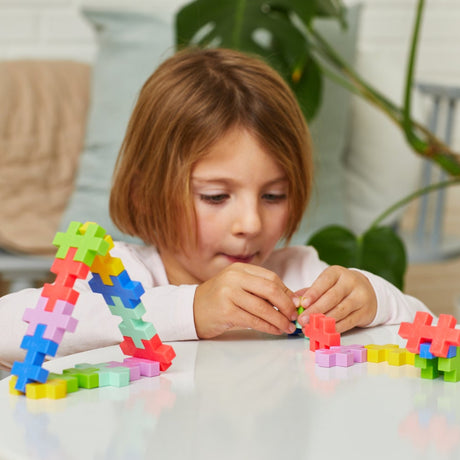 Young girl focused on assembling colorful Plus-Plus BIG tropical blocks at a white table.