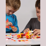 Two children focus intently on assembling colorful interlocking toy bricks at a white table. A completed car model is visible, creating an absorbed and playful atmosphere.