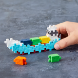 A hand holding an abstract boat model made of colorful interlocking puzzle pieces on a gray surface. Loose pieces, orange and green, lie nearby.