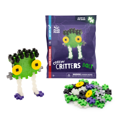 Toy packaging for "Plus-Plus Creepy Critters Bolt" featuring colorful interlocking pieces. A completed monster with green face, big yellow eyes, and white legs is assembled beside a pile of loose pieces. Glow-in-the-dark feature highlighted.