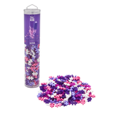 A clear tube labeled "Plus Plus Glitter" filled with pastel pink, purple, and white connecting pieces stands upright. A pile of pieces sits beside it.