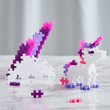 Plastic construction blocks form a white unicorn with pink and purple accents on a marble surface, conveying a playful and whimsical tone.