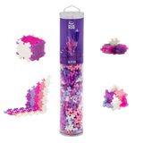 Tube of Plus-Plus glitter building blocks with pink, purple, and white pieces arranged in various shapes, set against a white background.