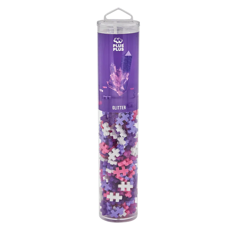 Tall, clear tube with colorful interlocking plastic pieces in purple, pink, and white. The purple label reads "Plus-Plus Glitter" and features crystal graphics.