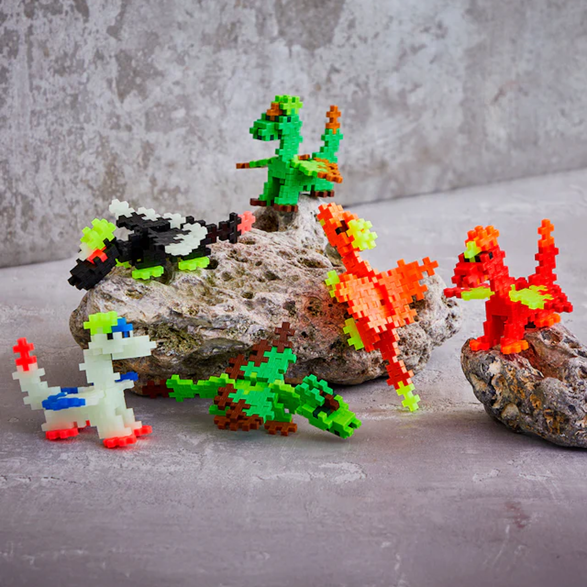 Colorful pixelated dinosaur figures on gray rocks against a concrete wall backdrop. The scene is playful and vibrant, highlighting creativity.