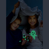 Two children smile under a blanket fort, holding glowing pixel-shaped toys in a cozy, playful setting. The mood is joyful and imaginative.