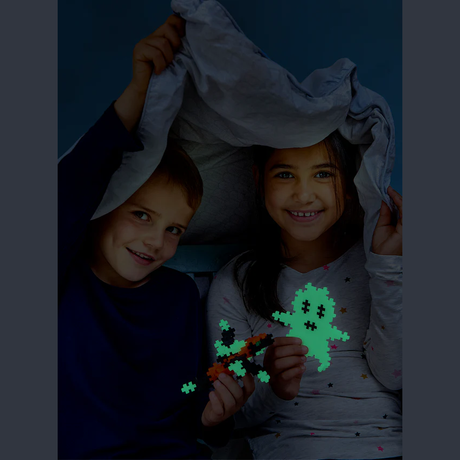 Two children smile under a blanket fort, holding glowing pixel-shaped toys in a cozy, playful setting. The mood is joyful and imaginative.