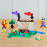 Plus-Plus blocks used to build a colorful castle, landscape, and figures on a wooden table. 600-piece basic set.