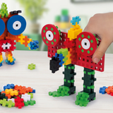 Colorful Plus-Plus block creatures and loose building pieces on a white table with a child's hand.