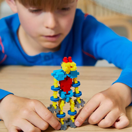 A child building a colorful robot out of Plus-Plus blocks on a wooden table. STEM educational toy for creative play.