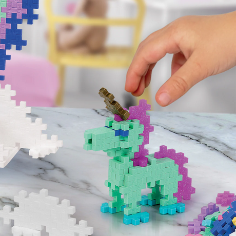 Plus-Plus unicorn building toy made of teal and purple blocks on a marble surface, featuring a gold horn.