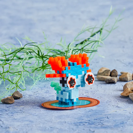 Colorful toy creature made of interlocking blocks, with orange and blue elements, large eyes, and abstract foliage and stones in the background. Playful tone.