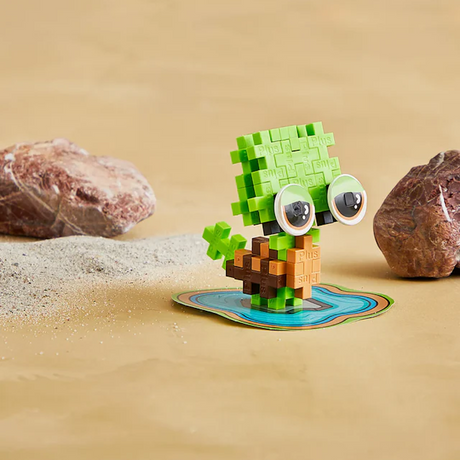 Toy turtle made of interlocking blocks with big eyes, standing on a small blue platform on sandy ground. Two rocks flank the turtle, creating a playful scene.