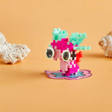 Colorful toy creature made of interlocking blocks on an orange surface, featuring large eyes and small wings. Coral pieces rest nearby, creating a playful scene.