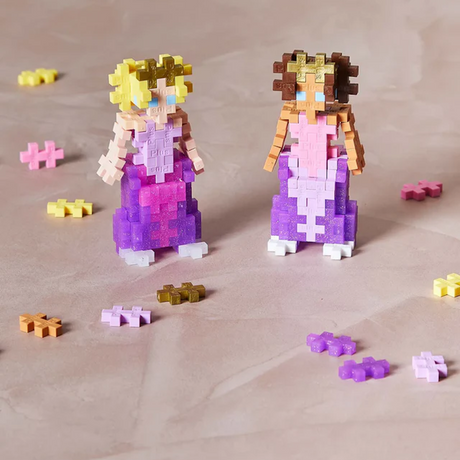Two blocky princess figures made of interlocking pastel blocks, one with blonde hair and the other brown, stand on a textured surface with scattered blocks.