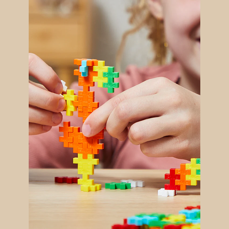 Child's hands building with colorful interlocking blocks, sculpting an abstract figure on a wooden table. The scene conveys creativity and joy.