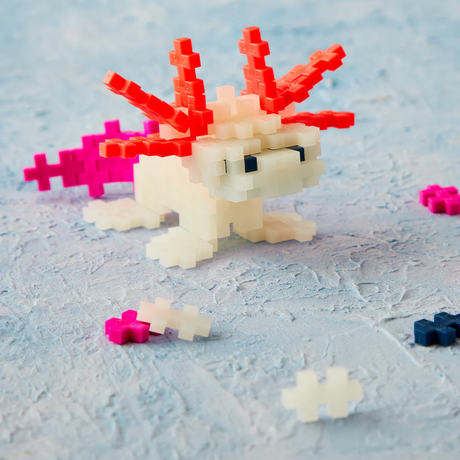 White axolotl figure made of Plus-Plus blocks with red gills and pink tail on a textured blue surface.