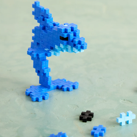Blue dolphin made of Plus-Plus blocks standing on a green surface with scattered blue and black pieces.