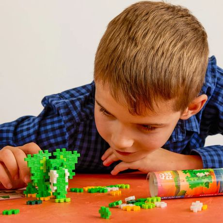 Young boy building a green elephant with Plus-Plus construction blocks on an orange surface.
