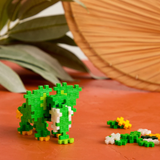 Green Plus-Plus block elephant with white tusks on an orange surface with scattered building pieces.