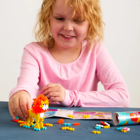 A young girl playing with a Plus-Plus lion toy building set, featuring colorful interlocking blocks on a blue table.