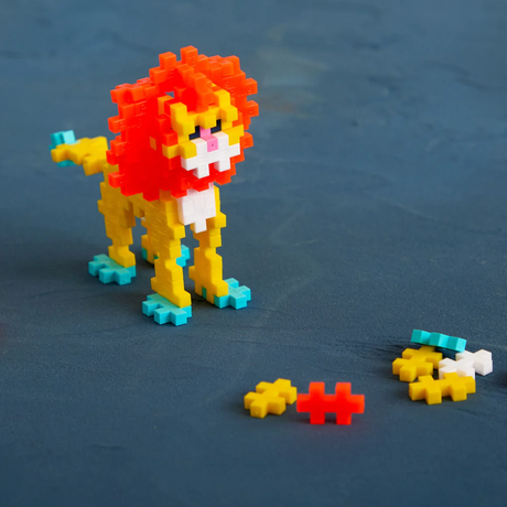 A colorful lion toy built with Plus-Plus blocks standing on a blue surface with extra building pieces nearby.