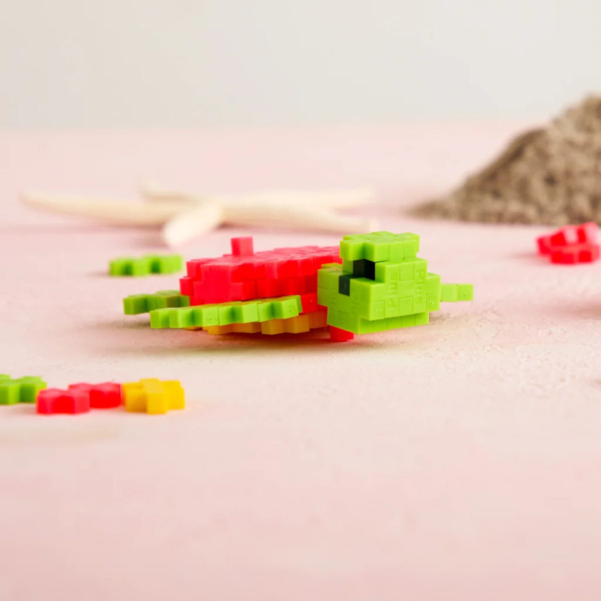 A lime green and coral pink sea turtle made of Plus-Plus blocks on a pink sandy surface with a starfish background.