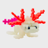 Plus-Plus axolotl building set figure with glow-in-the-dark white body, pink gills, and a purple tail on a gray background.