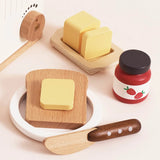 Wooden toy breakfast accessories including a butter dish, toast on a plate, strawberry jam, and a knife.