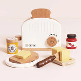 Wooden toy toaster set with a slice of bread, butter, a knife, honey, and strawberry jam on a neutral background.