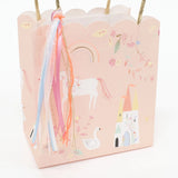 Pink gift bag with a scalloped edge, featuring a unicorn, castle, swan, and hanging colorful ribbons.