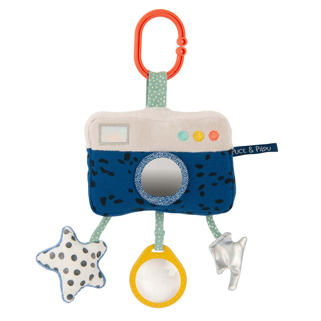 Plush camera-shaped baby toy with polka dots features a red ring clip, a mirror lens, and dangling star, circle, and arrow shapes in soft colors.