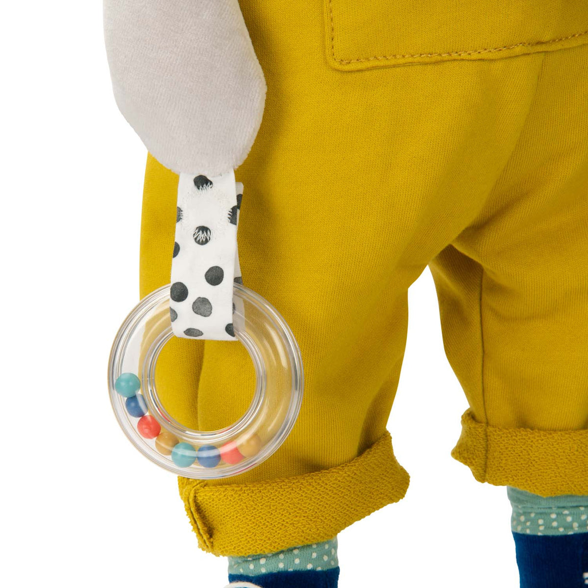 Close up of a clear plastic ring rattle accessory on a plush dog activity toy in yellow overalls.