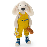 Plush dog toy wearing yellow overalls and blue shoes holding a rattle.