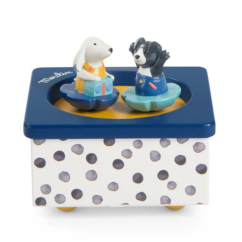 Toy music box with a dotted base, featuring a white rabbit and black dog figure in colorful outfits. They appear to dance on a blue platform.