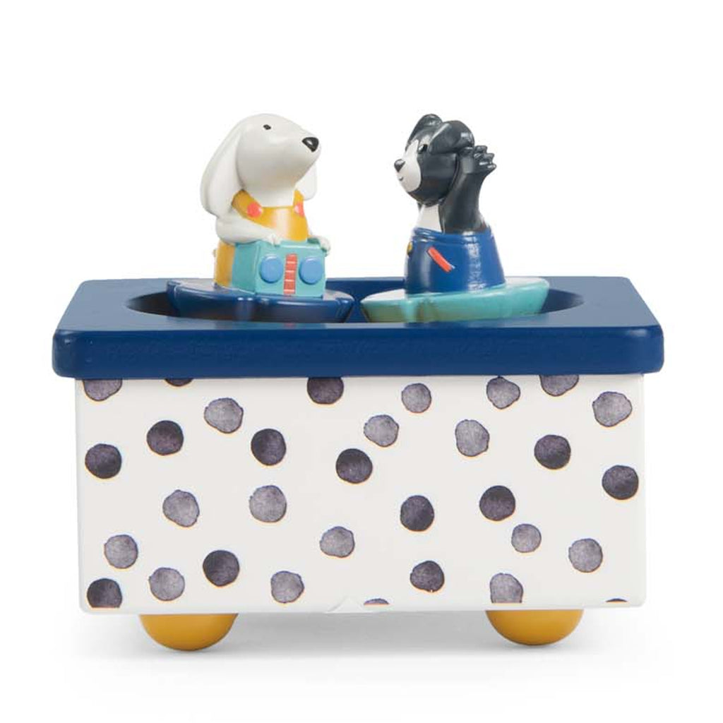 Toy music box with a dotted base, featuring a white rabbit and black dog figure in colorful outfits. They appear to dance on a blue platform.