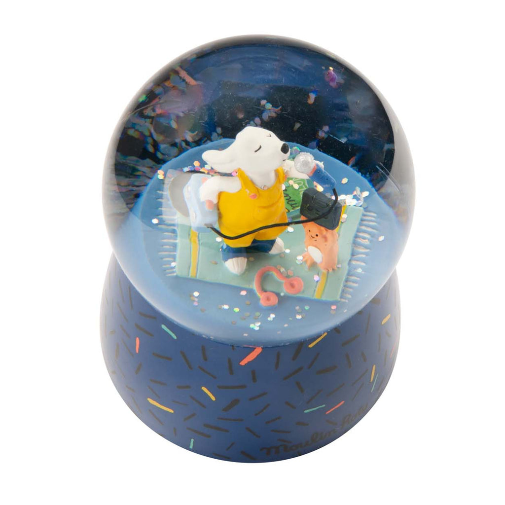 A whimsical snow globe featuring a white dog in yellow overalls singing with a blue microphone. It stands on a blue base with colorful sprinkles.