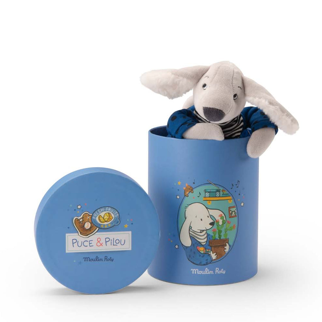 Cute plush dog with floppy ears wearing a striped shirt and blue pants, sitting in a blue cylindrical box with playful illustrations and text.