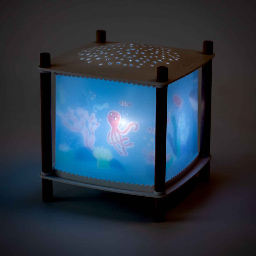 A glowing cube nightlight with an underwater theme. An octopus and fish are visible on its sides, and star-like patterns are projected above.