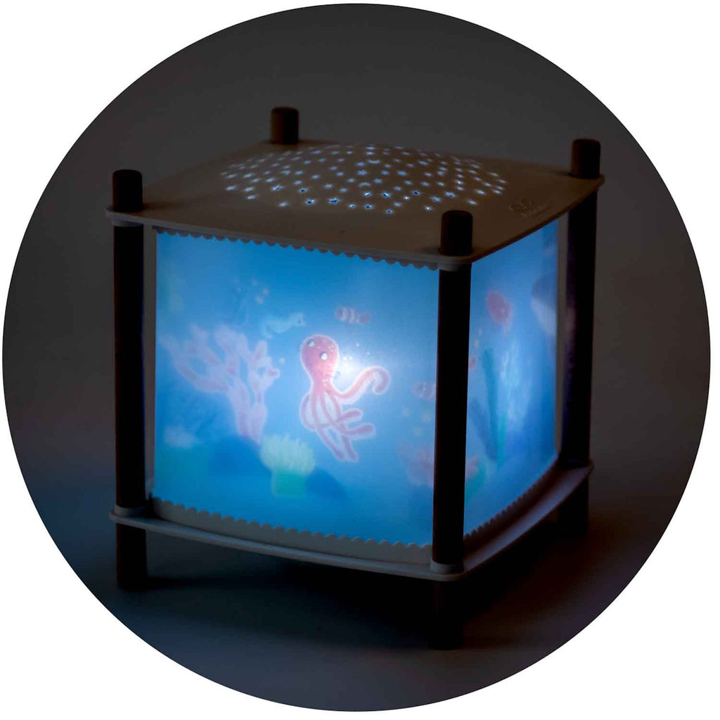 A glowing cube nightlight with an underwater theme. An octopus and fish are visible on its sides, and star-like patterns are projected above.